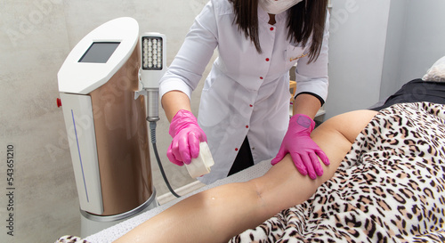 The masseur applies oil to the patient leg skin for massage with anti-cellulite machine photo