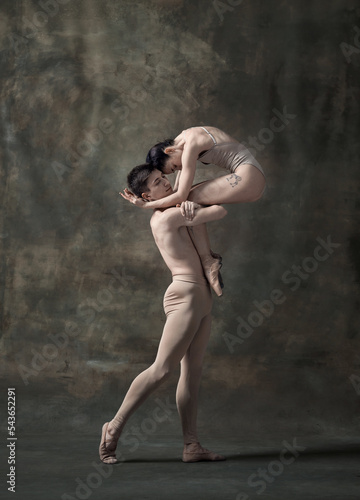 Young man and woman, ballet dancers performing isolated over dark green vintage background. Romantic look