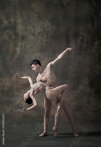Young man and woman, ballet dancers performing isolated over dark green vintage background. Affection