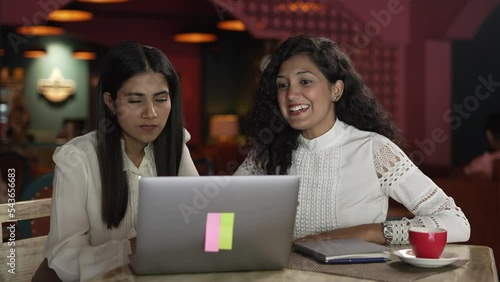 Two Indian business female group of girls working on online project together,discussing and streaming on laptop while successful project good news and other girl bad news siting on laptop in the cafe. photo