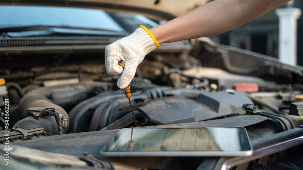A repairman is checking car engine motor oil level, using the checklist document in the digital tablet device. Industrial and transportaion occupation working scene, selective focus. A repairman is checking car engine motor oil level, using the checklist document in the digital tablet device. Industrial and transportaion occupation working scene, selective focus.