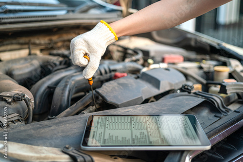 A repairman is checking car engine lube oil level, using the checklist document in the digital tablet device. Industrial and transportaion occupation working scene, selective focus.