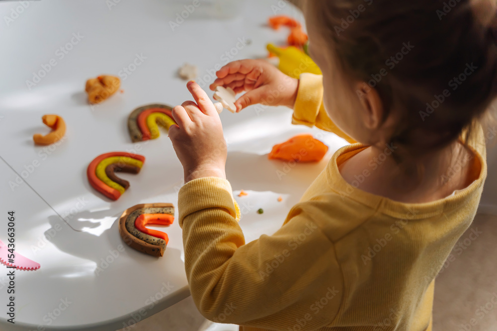 A little girl playing with rainbow from play dough for modeling. Art Activity for Kids. Fine
