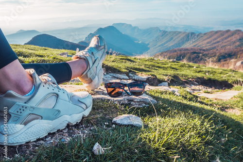 Woman's legs lying on top of the mountain. Rest after reaching the top of the mountain. Close-ups of sunglasses in the mountains. Women's sunglasses in the mountains. Panorama view of the mountains 
