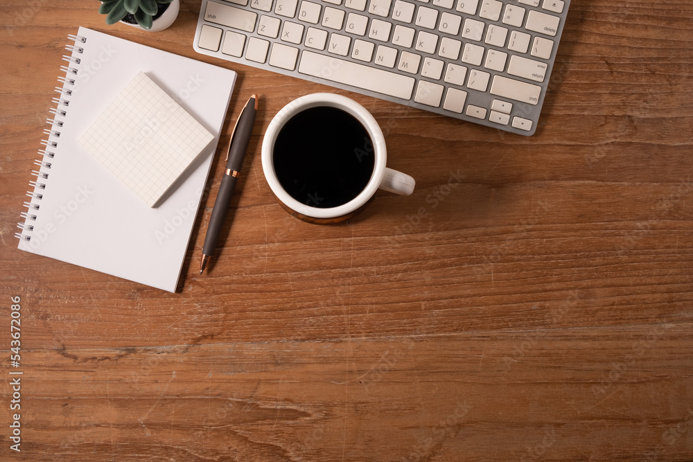 Above view of coffee cup, notepad, pen and keyboard on wooden table. Above view of coffee cup, notepad, pen and keyboard on wooden table.