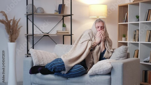 Cold aged man. Heating system. Low temperature. Casual elder male in pajamas suffering and trembling covering plaid on sofa light room interior. photo