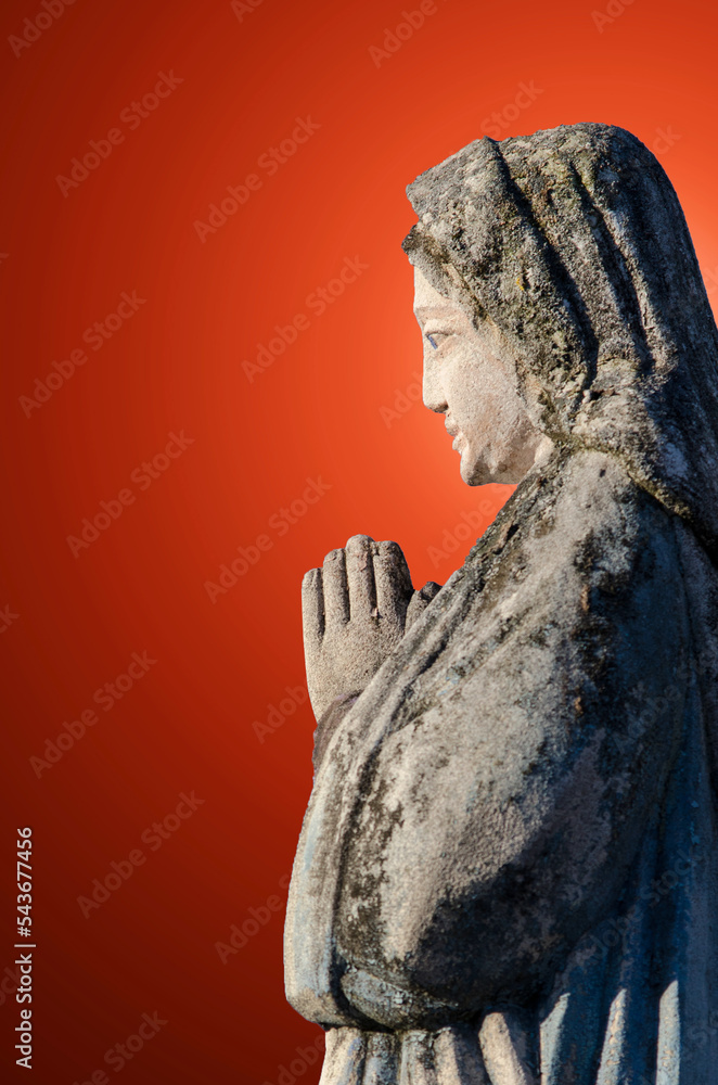 An ancient sculpture of the Virgin Mary with folded hands in prayer against the background of rays of light, which symbolize the personification of the Holy Spirit.