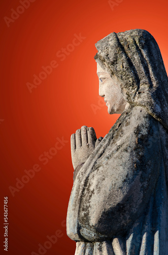 Obraz na płótnie An ancient sculpture of the Virgin Mary with folded hands in prayer against the background of rays of light, which symbolize the personification of the Holy Spirit. w salonie