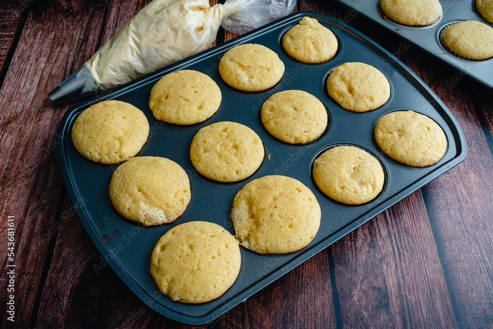 Foto de Vanilla Cupcakes in a Muffin Pan with a Piping Bag of