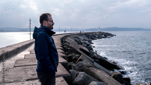 Lonely man watching open sea in harbor, thoughtful gaze, dark clouds and sea, winter weather, image with text space