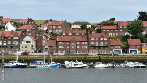 LANDSCAPE OF WHITBY TOWN NEAR THE RIVER  , RED BROWN HOUSES ,ROOF TILE AND WHITE FRAME WINDOWS AND  FISHING BOATS AT DOCK.UK URBAM PLANNING photo