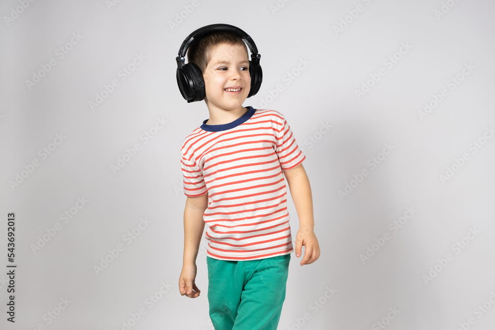A happy 5 year old boy in large black headphones smiles and looks away on a white background, a place for text copy space A happy 5 year old boy in large black headphones smiles and looks away on a white background, a place for text copy space