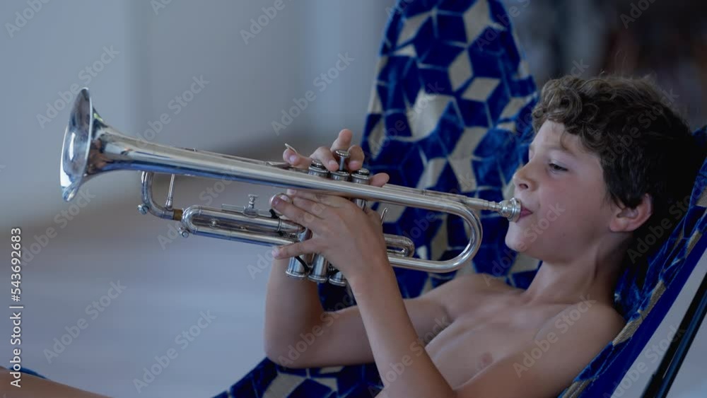 One young boy playing trumpet. Preteen male kid practicing musical instrument indoors shirtless