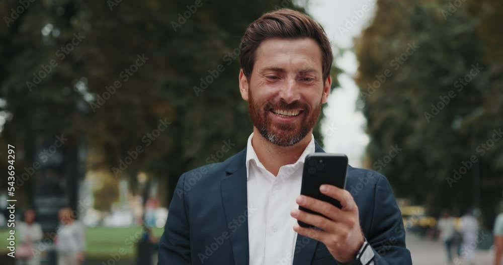 Smiling middle aged businessman browsing smartphone, walking on city alley Smiling middle aged businessman browsing smartphone, walking on city alley