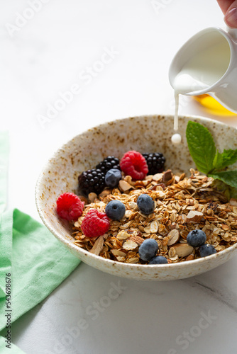 grains granola with fresh berries in white bowl breakfast food concept blueberry vegan milk pouring