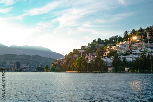 Beautiful panoramic view of Lugano town and the green Swiss Alps in the background visible from Lake Lugano side during sunset. Canton of Ticino, Switzerland.