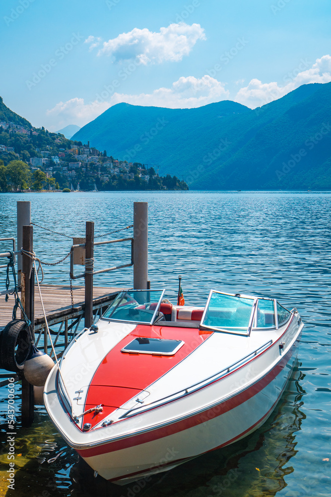 Stunning luxury speed boat moored at the shore of Lake Lugano on a sunny summer day, with the green lush Swiss Alps in the distance, Lugano, Switzerland.