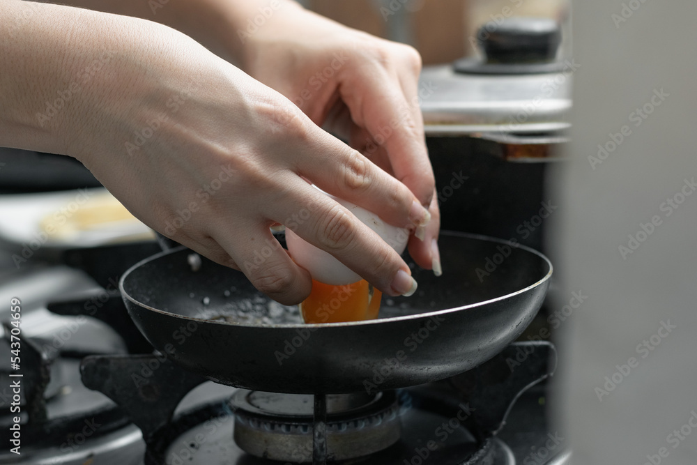 detailed shot of a girl's hands opening an egg and pouring it into the small frying pan to prepare the typical Colombian breakfast.