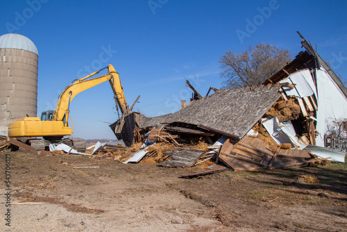 Close up view of an old abandoned barn building being demolished with a heavy equipment excavator