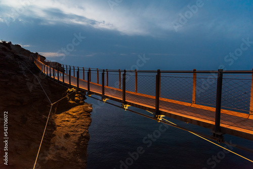 Jolucar suspension footbridge, in Torrenueva Costa, Granada, view of the footbridge before dawn with the wooden floor illuminated, and the cloudy sky. photo