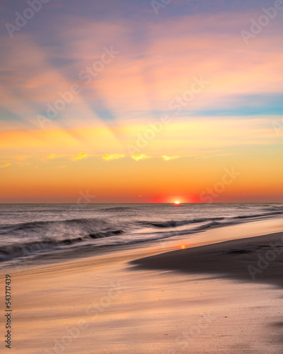 Vibrant sunset over the ocean as the sun dips below the horizon creating crepuscular rays and sunbeams . Long Island New York photo