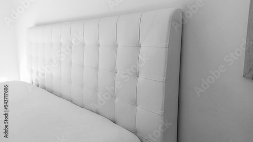 Soft headboard. Upholstery for furniture made of genuine or artificial leather and quilted fabric. Soft headboard against a light wall. Black and white monochrome photo