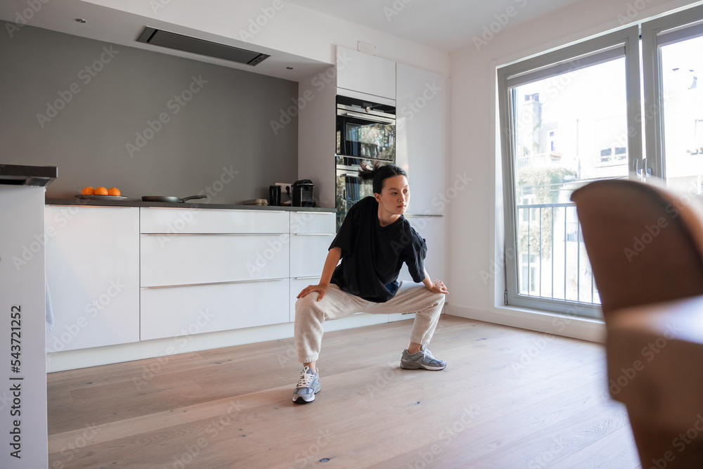 Brunette focused balanced lady standing and stretching at the kitchen at home Brunette focused balanced lady standing and stretching at the kitchen at home