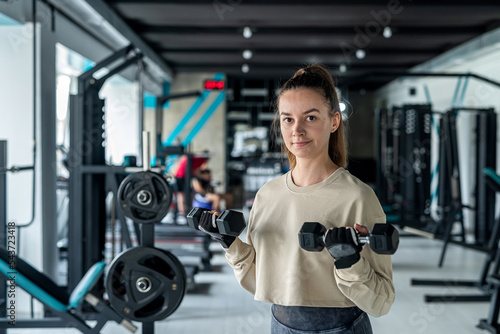girl in training with heavy large dumbbells trains arm endurance.