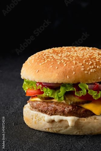 Close up classic traditional cheeseburger with beef, tomato, lettuce, pickles and onion on black background