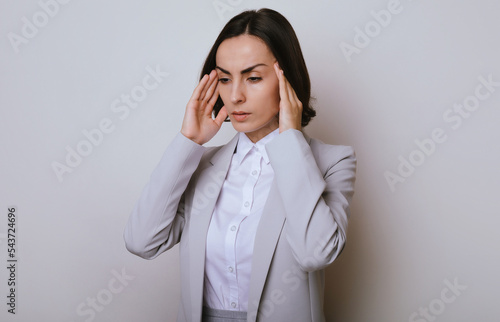 Young business woman isolated over gray background is suffering from severe headache, desperate and stressed because pain and migraine after troubles on work