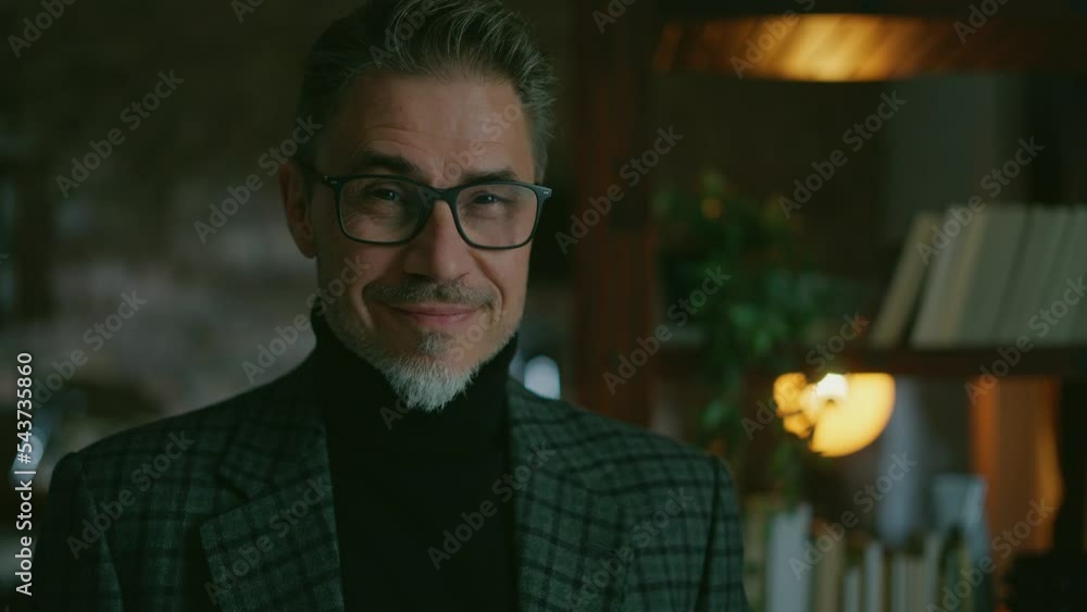 Portrait of happy 40s or 50s man at home in turtleneck pullover and jacket. Middle aged, mid adult, mature age teacher in glasses, smiling. Older guy standing in dark loft room. Portrait of happy 40s or 50s man at home in turtleneck pullover and jacket. Middle aged, mid adult, mature age teacher in glasses, smiling. Older guy standing in dark loft room.