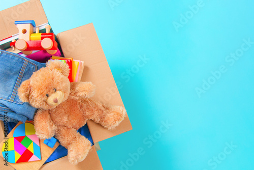 Fotobehang Donation box with kid toys, books, clothing for charity on light blue background