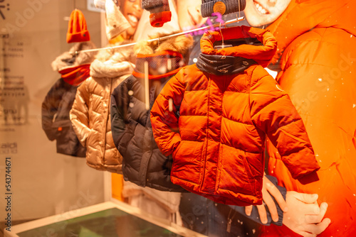 Men's and women's clothing store. Three mannequin dressed in parka, jackets, hat, behind the glass. Display of a clothing store