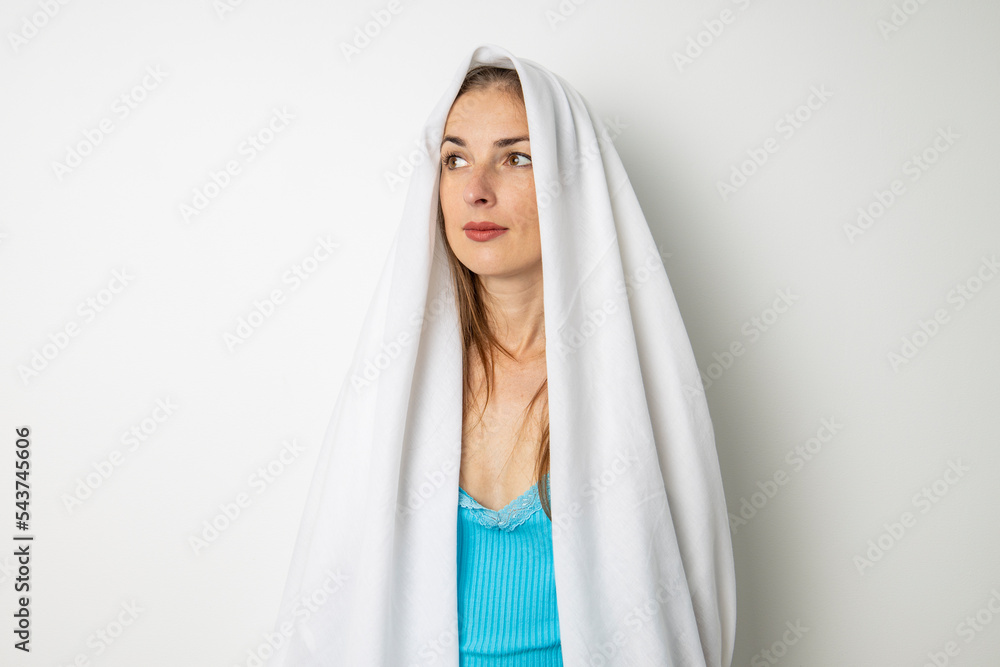 Young woman covering her head with a white sheet on a white background Young woman covering her head with a white sheet on a white background