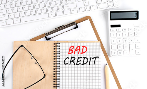 Notebook with the word BAD CREDIT with keyboard and calculator on the white background photo