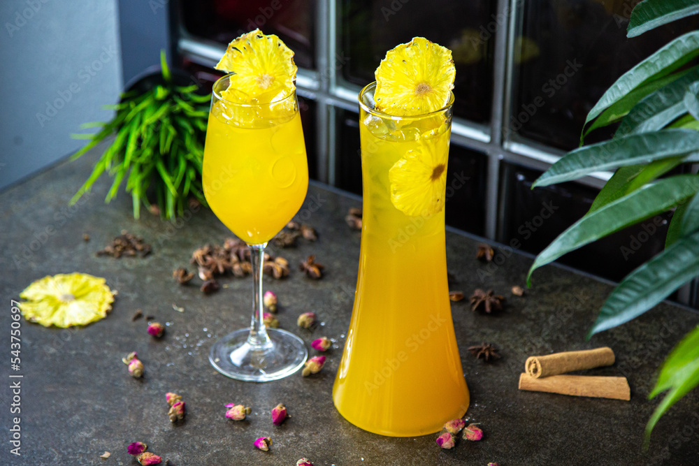 homemade lemonade with the taste of tropical fruits in a glass or decanter. Lemonade with ice in a yellow glass. Lemonade is decorated with pineapple slices and stands on a decorated table. side view