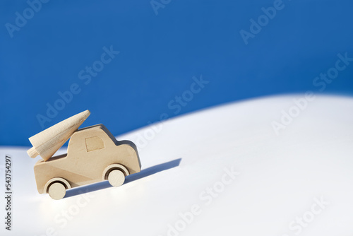 Wooden toy, silhouette of Christmas tree on toy car on colored layered paper background. Xmas holiday blue celebration background. Copy-space, place for text, greeting. Simple, minimal design.