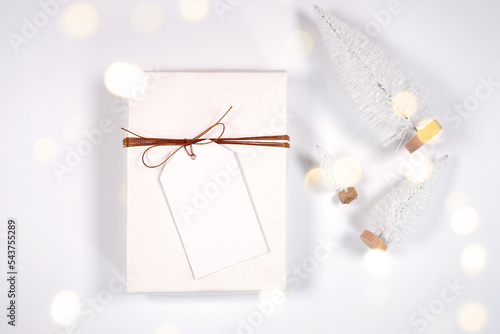 Christmas gift tag party favor thank you card mockup, styled with white reindeer and mini trees, bokeh party fairy lights on a minimalist white background. photo