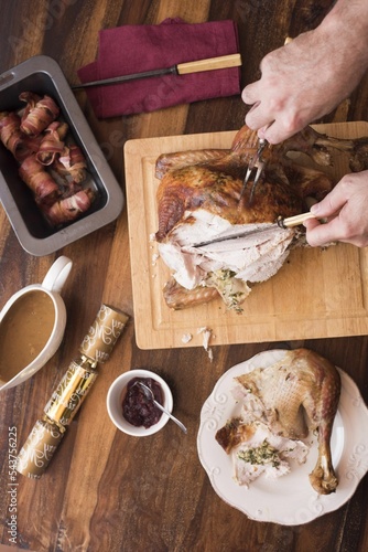 Vertical high angle shot of a person carving a delicious turkey on a wooden board on the table