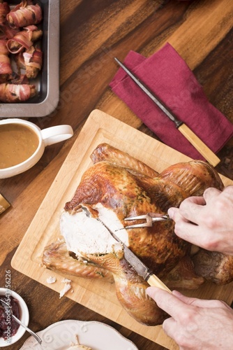 Vertical top view of a person carving a delicious turkey on a wooden board on the table