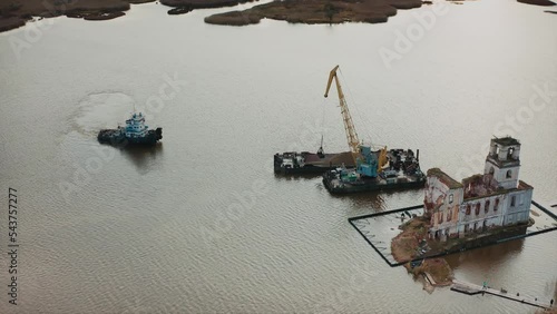 The tugboat sails to the barge, from which the crane unloads the sand. Aerial drone shot photo