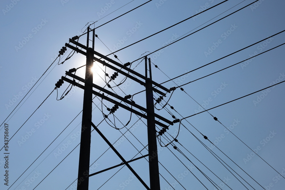 Silhouette of twin electric poles. Dark shadow of concrete power pole paired with high voltage cable with insulator and Guy Wire pulling pole on clear sky background with afternoon sun shining with co Silhouette of twin electric poles. Dark shadow of concrete power pole paired with high voltage cable with insulator and Guy Wire pulling pole on clear sky background with afternoon sun shining with co