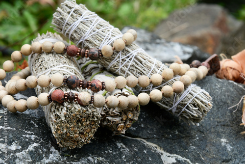 A close up image of three healing smudge sticks with wooden mala beads.