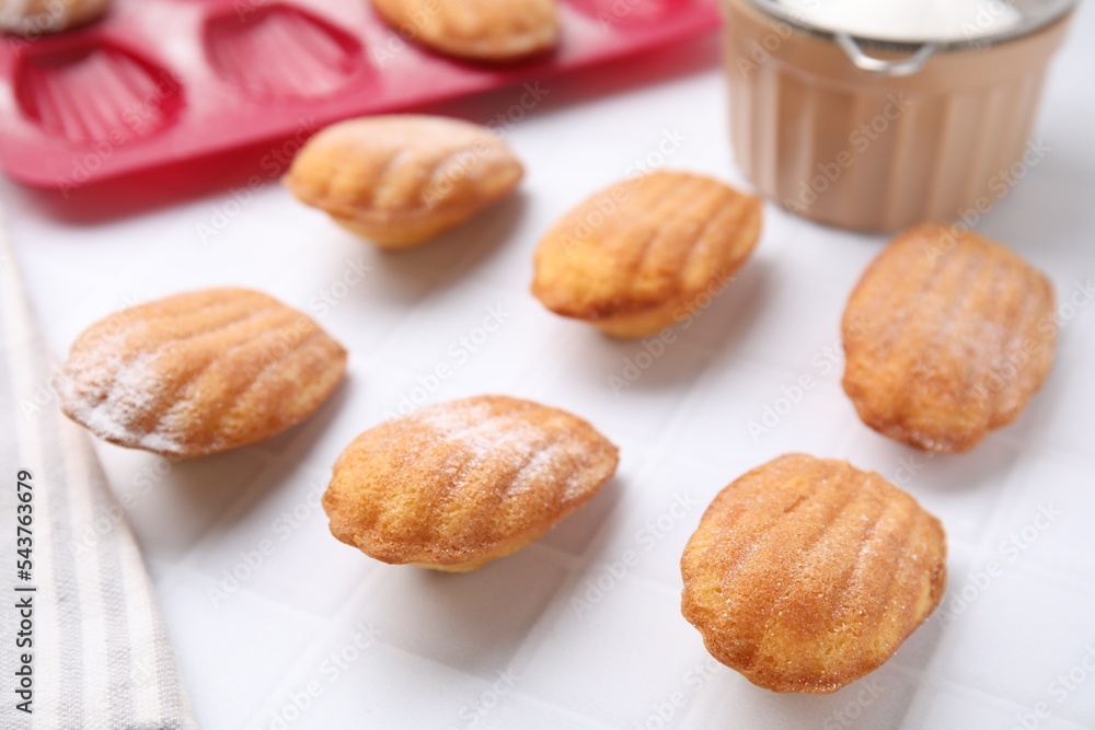 Delicious madeleine cookies and baking mold on white tiled table, closeup