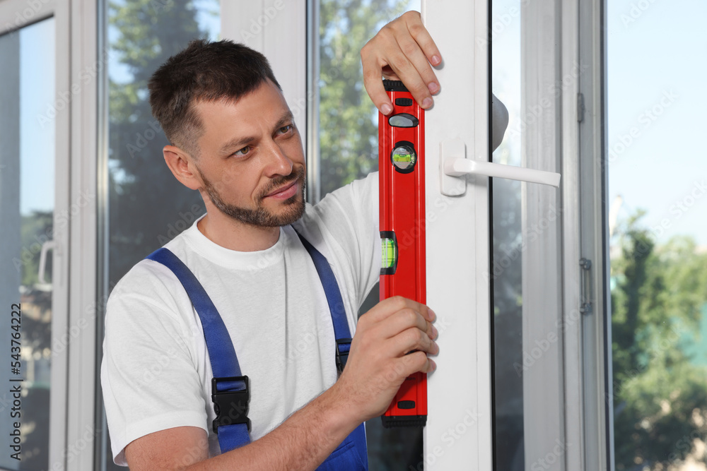 Worker using bubble level after plastic window installation indoors Worker using bubble level after plastic window installation indoors