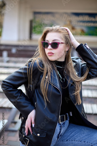 Outdoor portrait of a beautifull young woman in a black jacket and pink sunglasses