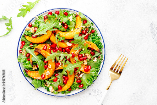 Autumn pumpkin salad with baked honey pumpkin slices, lettuce, arugula, pomegranate seeds and walnuts. Healthy vegan eating, comfort food. Top view