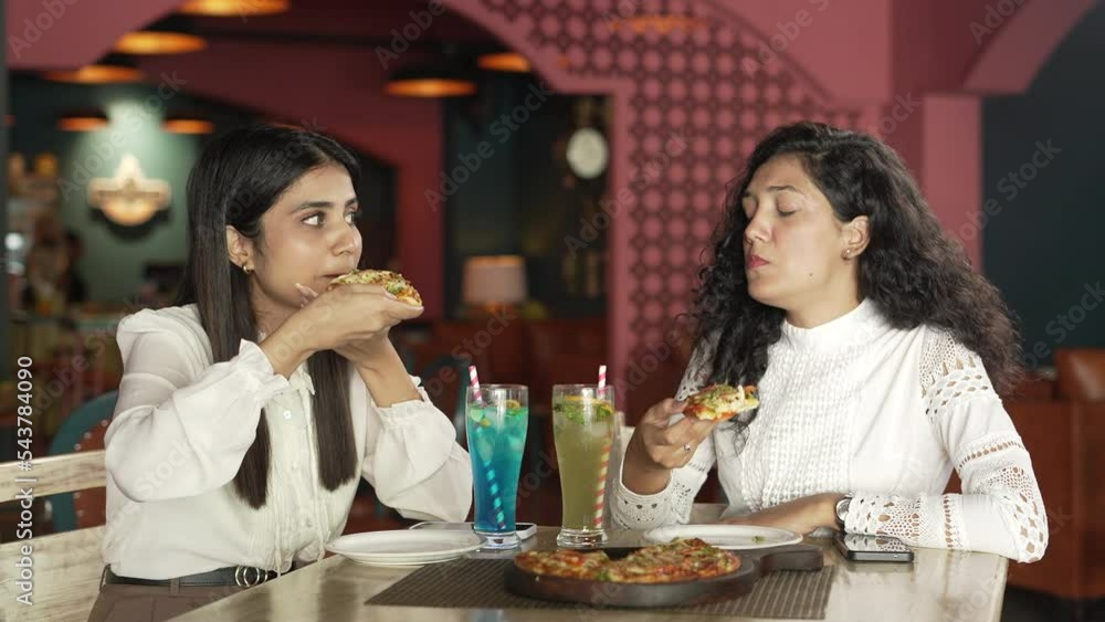 Group of young beautiful Indian woman sitting on chair and eating pizza and talking about their general happy topic in the restaurant. smiling Asian woman eating tasty pizza and enjoying breakfast. Group of young beautiful Indian woman sitting on chair and eating pizza and talking about their general happy topic in the restaurant. smiling Asian woman eating tasty pizza and enjoying breakfast.