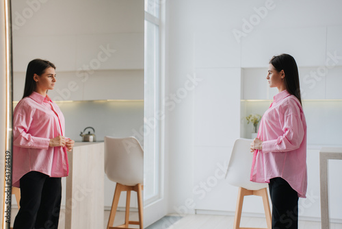 Canvas Print Sad brunette fit young woman in pink oversize shirt stands in front of mirror sees herself overweight