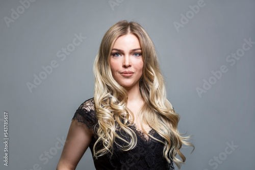 Beautiful smiling blonde in a black lace blouse. Elegance and sexy. Grey background.